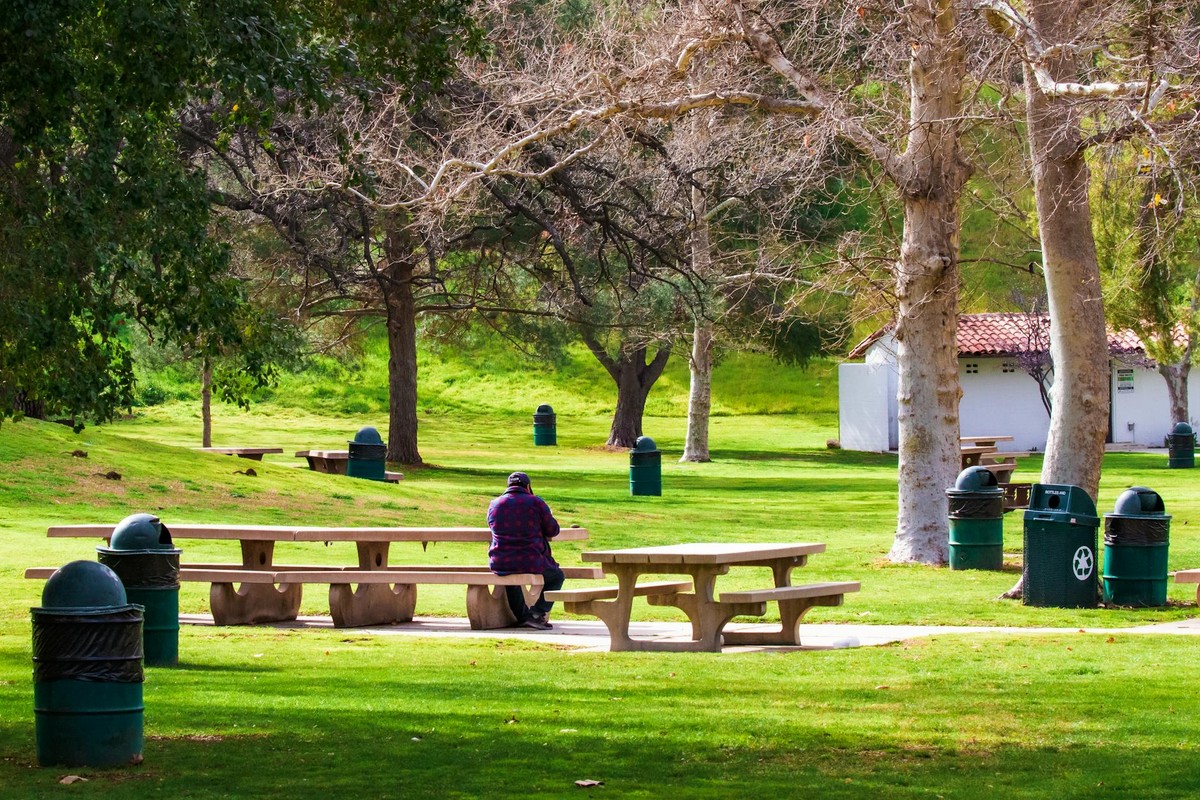 A person sitting alone on a bench in a green park on a sunny day in Santa Clarita, California.