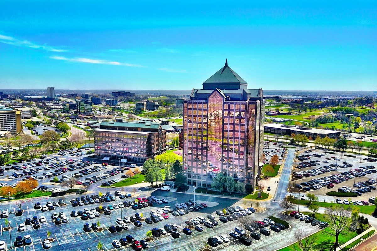 Bird's-eye view of a modern skyscraper and parking lot in Overland Park, KS, under a clear blue sky.