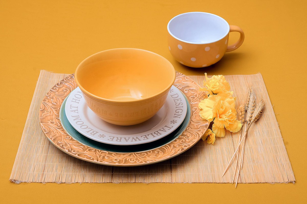 Elegant yellow ceramic dishes on a bamboo mat with flowers and wheat accents.