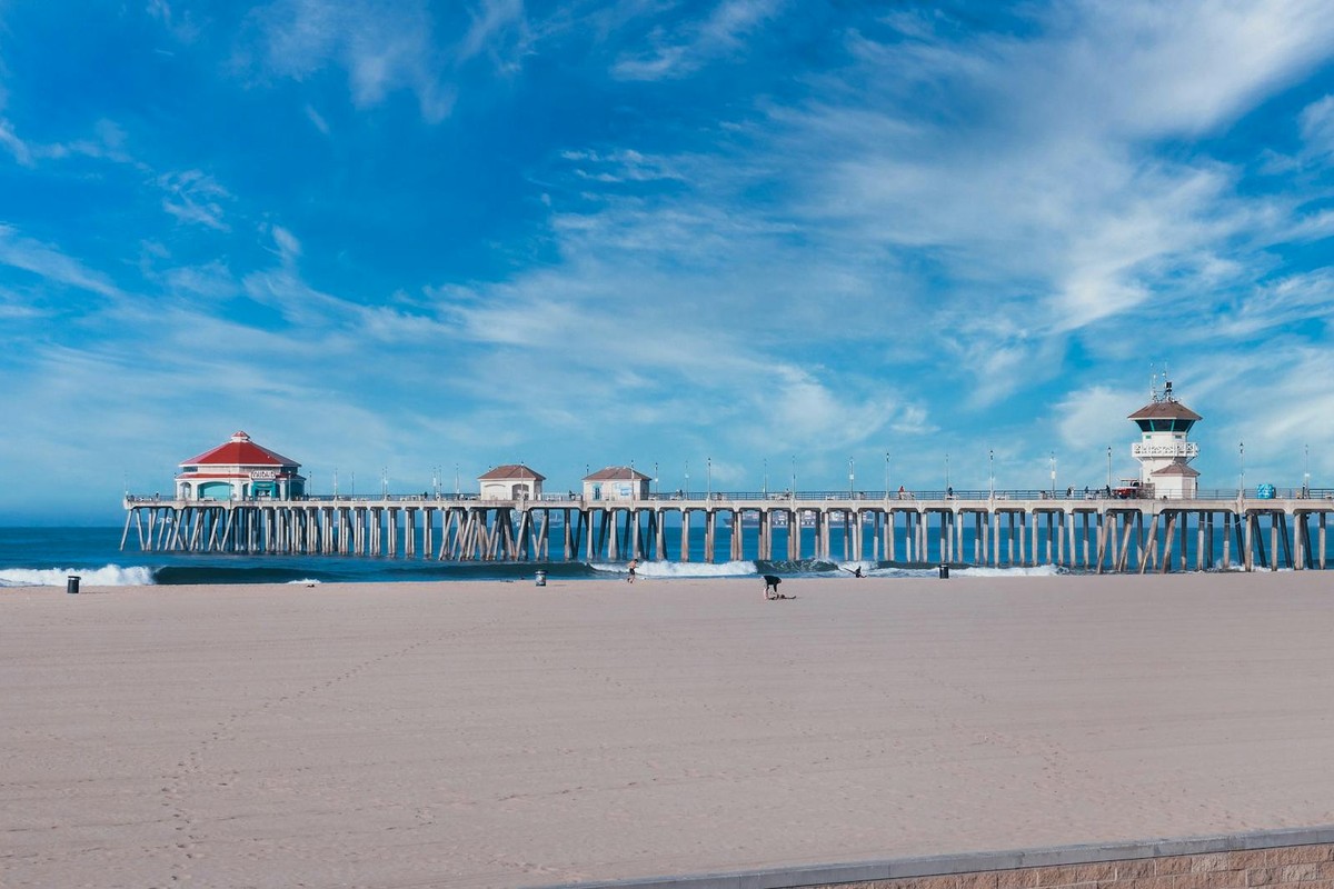 Huntington Beach Pier with blue sky, sandy beach, and ocean waves on a sunny day.
