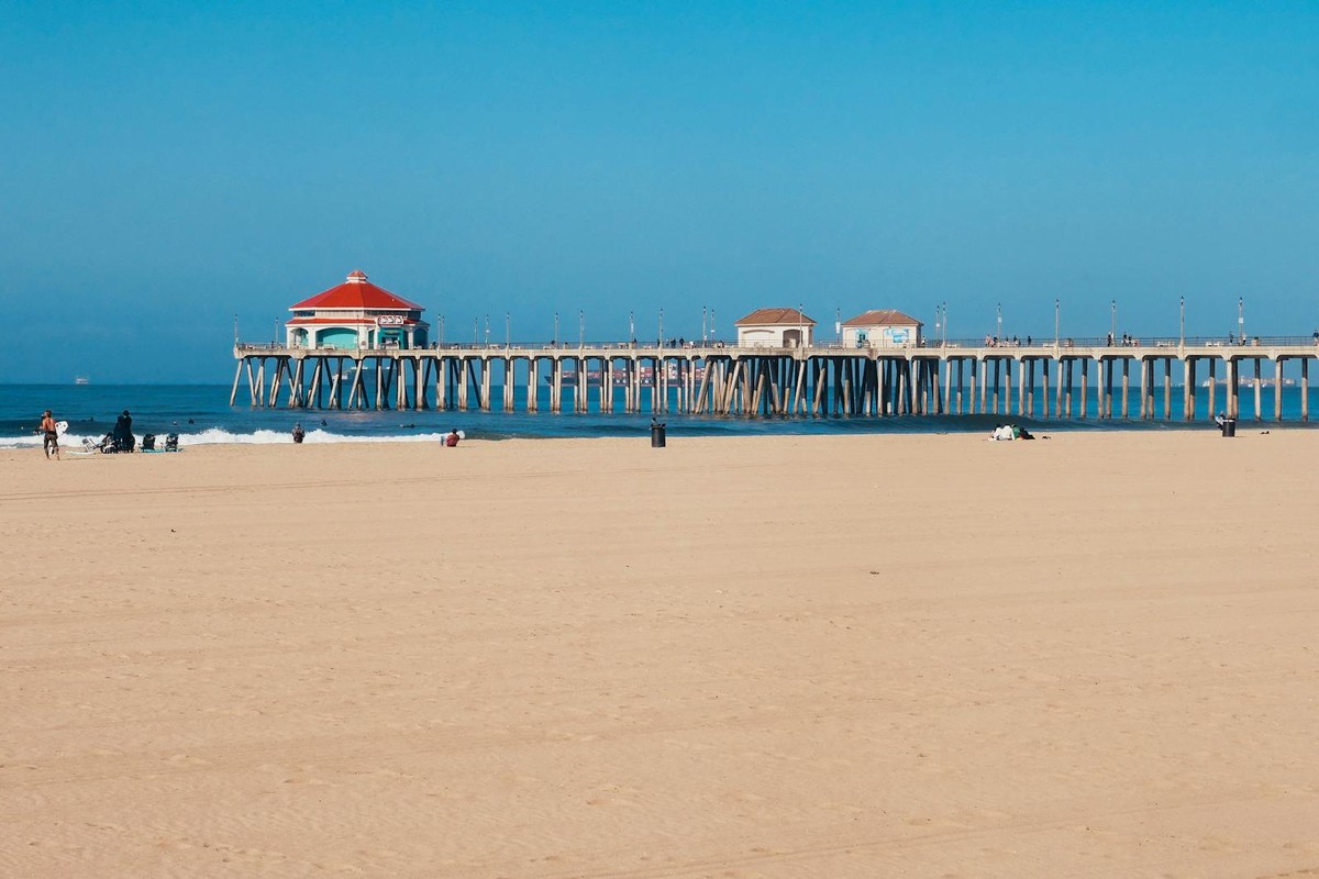 Sunny day at the beach with a distant pier and open blue sky, perfect for summer relaxation.