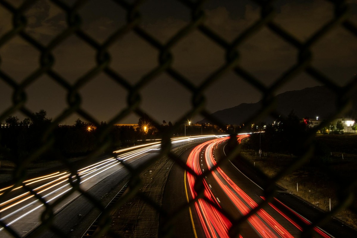 Night long exposure capturing car light trails through a chain link fence in Moreno Valley, CA.