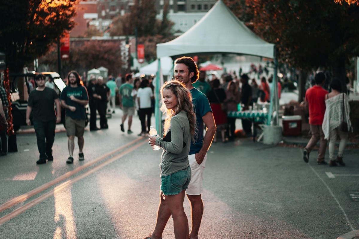 A couple enjoys a lively street festival in Fayetteville, Arkansas, surrounded by people and vibrant atmosphere.