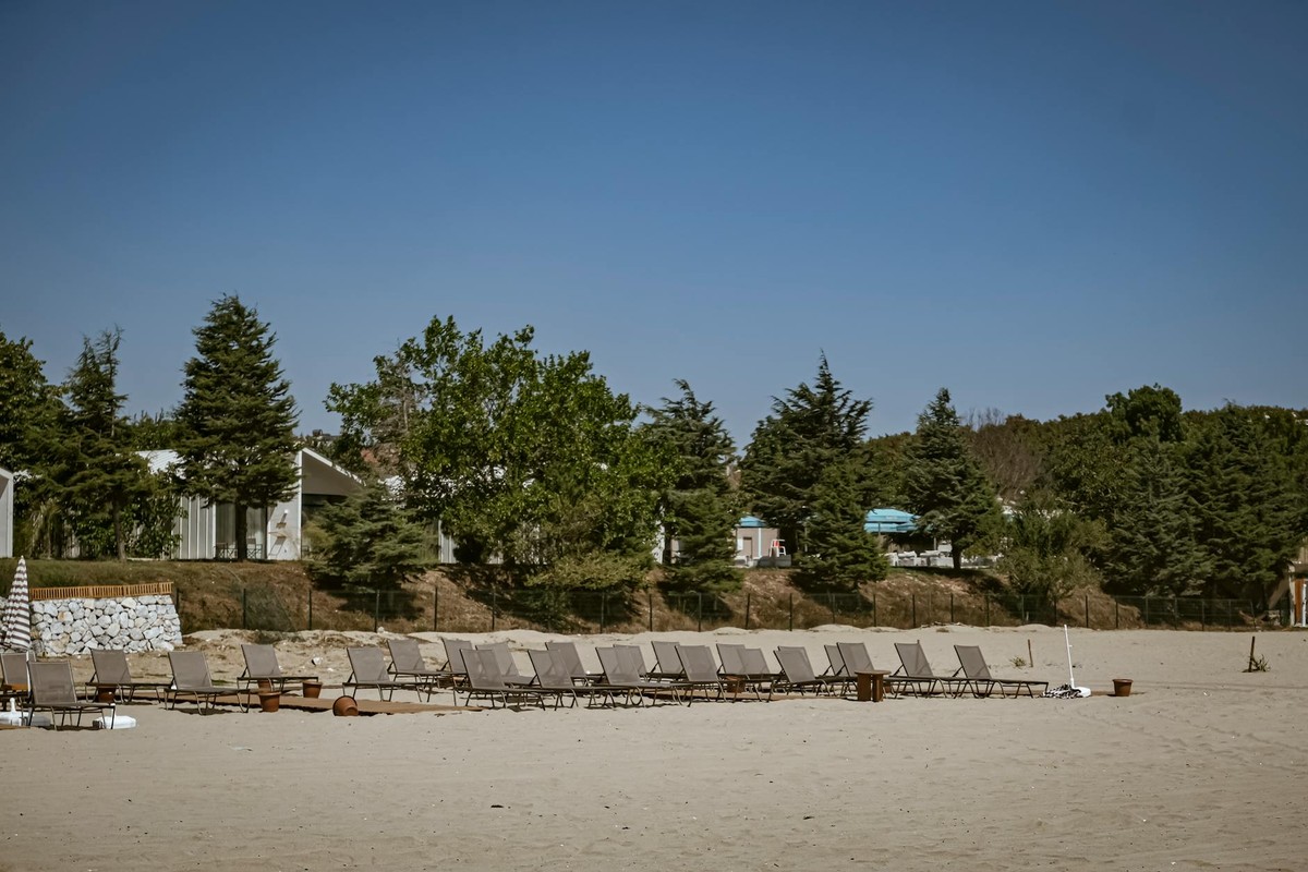 A serene beach in Igneada, Turkey with empty chairs under a clear sky, surrounded by lush greenery.