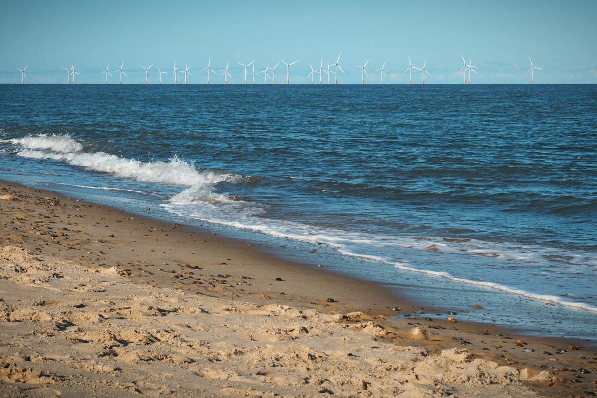 Idyllic Norfolk beach with serene waves and distant wind turbines under a clear sky.