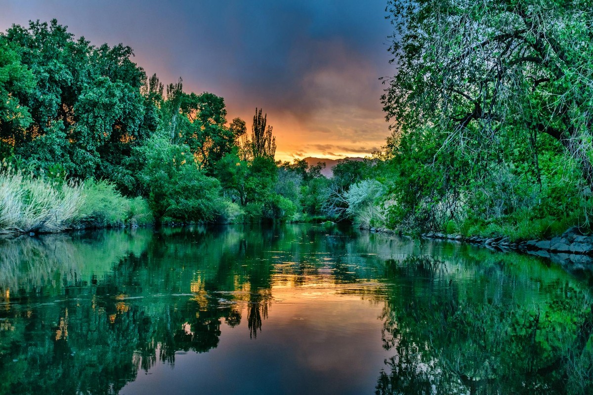 A tranquil river scene in Taylorsville, UT, showcasing lush greenery against a vibrant sunset sky.
