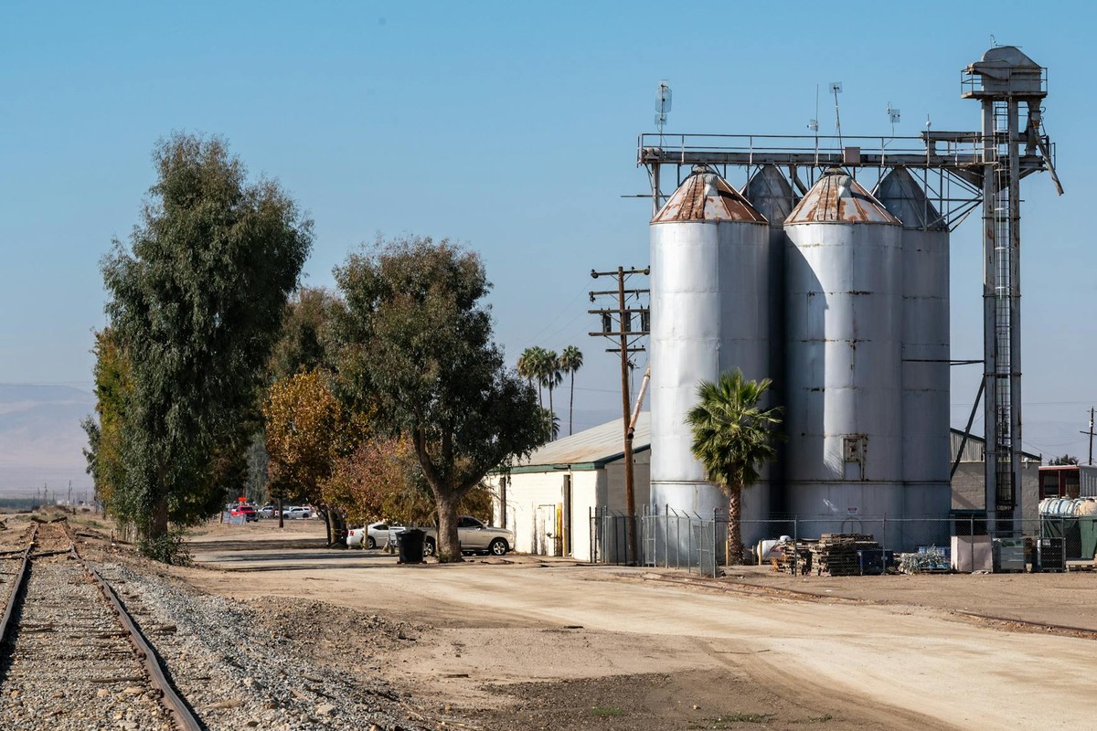 Industrial silos and railway tracks in a rural landscape under clear blue skies.