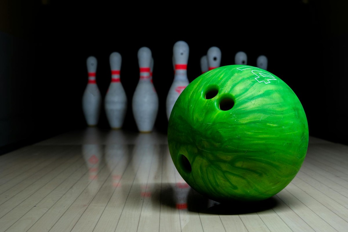 Close-up of a green bowling ball with pins ready to be knocked down.
