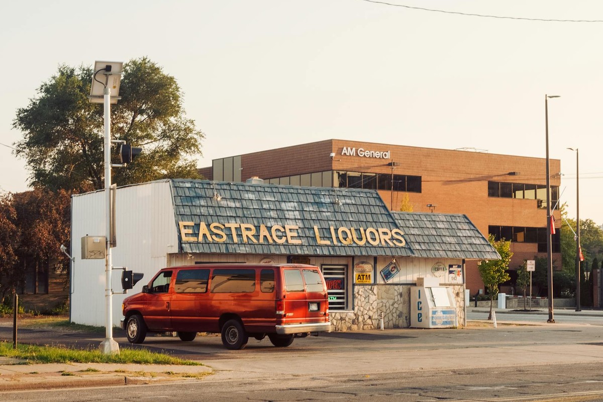 A vibrant street scene featuring a liquor store and parked vintage red van under a clear sky.
