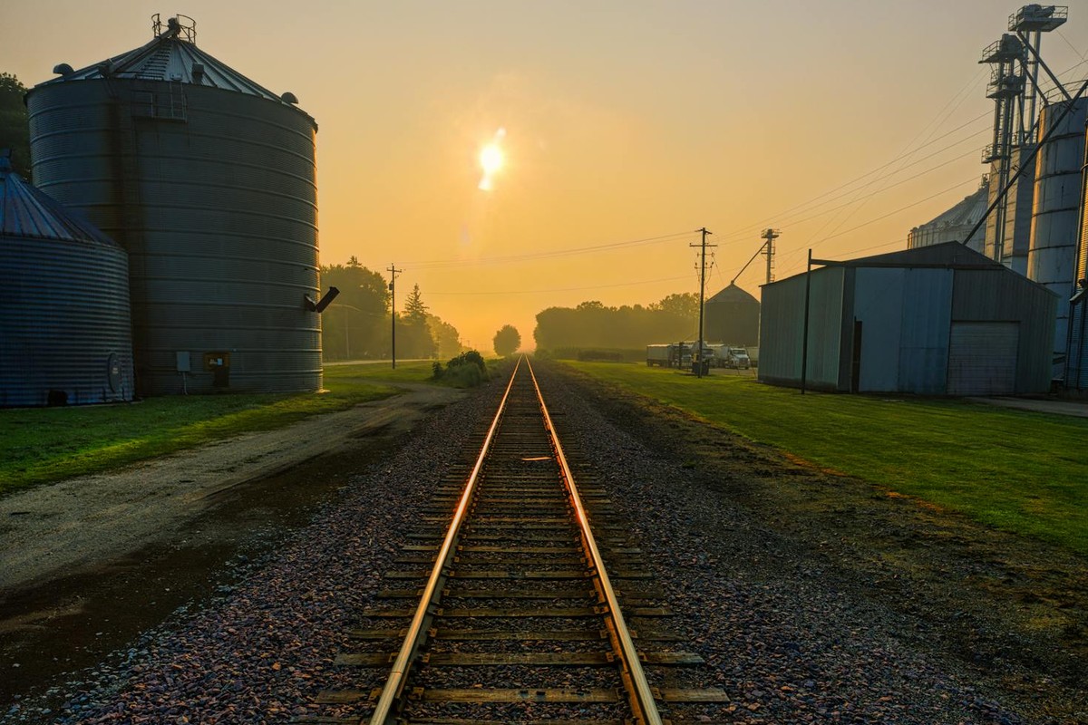 Golden sunrise over railroad tracks with silos in Utica, MN, creating a serene agricultural landscape.