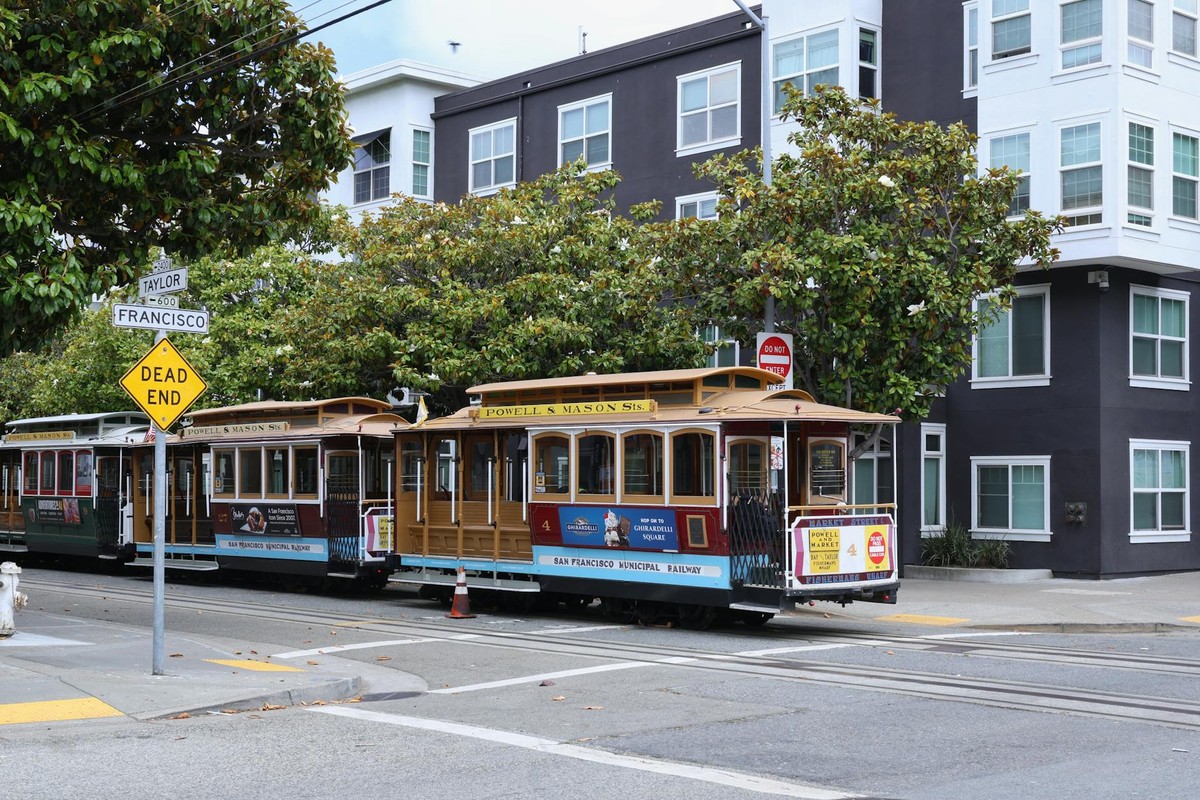 Classic San Francisco cable car on Powell and Mason, city streets, greenery, and iconic signs.