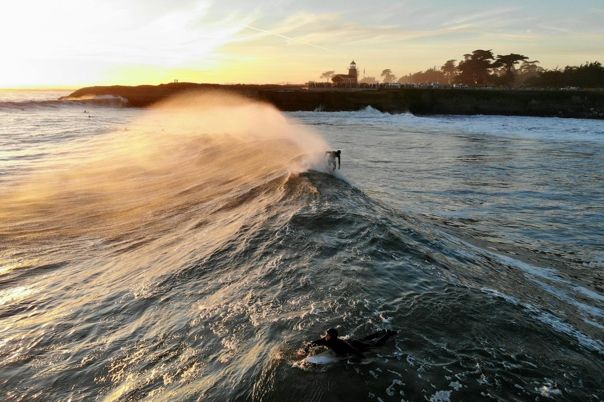 Breathtaking aerial view of surfers riding waves at sunset near the iconic lighthouse in Santa Cruz, California.