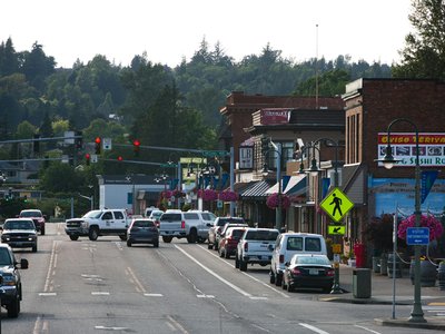 Lively urban street with cars, shops, and pedestrians during daytime.