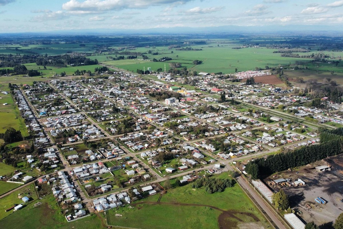 Aerial photo of a rural town surrounded by green fields under a cloudy sky, showcasing its layout.