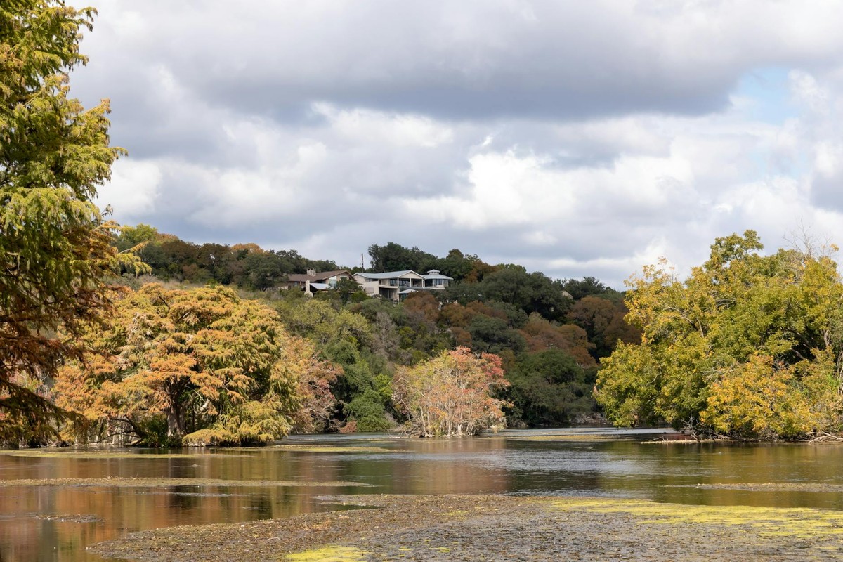 A serene autumn landscape of trees and a house by a lake in New Braunfels, Texas.
