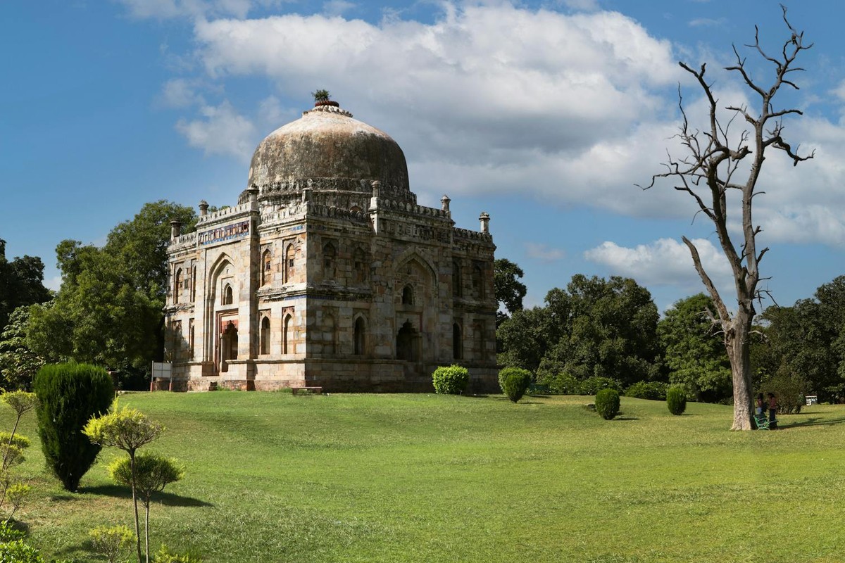 The historic Shish Gumbad tomb in New Delhi framed by lush gardens and a clear blue sky.