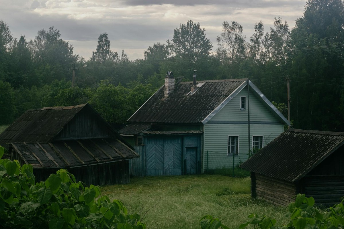 A tranquil rural scene featuring rustic homes surrounded by lush greenery under a cloudy sky.