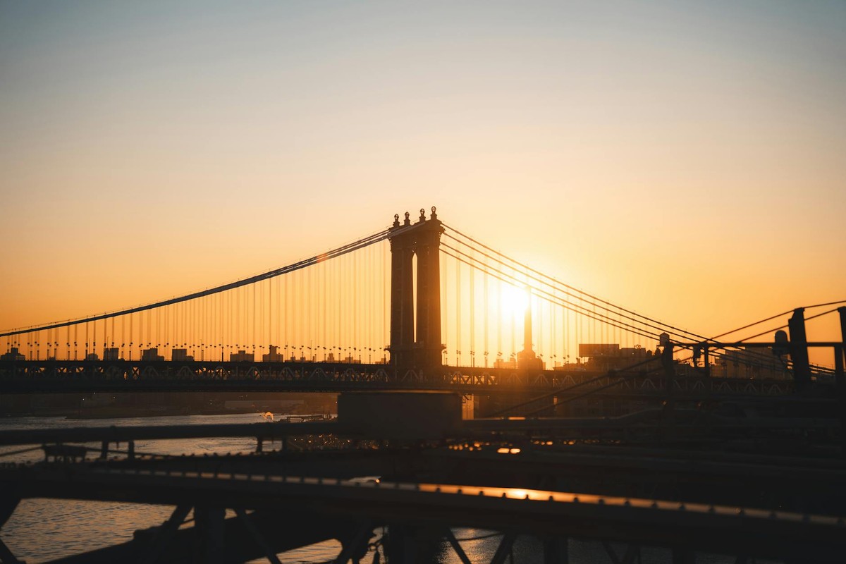 The sun rises majestically behind the iconic Manhattan Bridge, casting a warm glow over the New York City skyline.