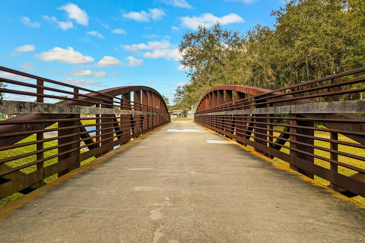 Wooden bridge in Kissimmee Park under a bright blue sky with clouds and trees.