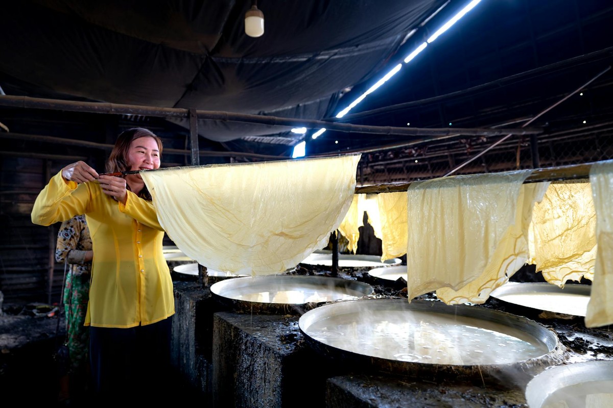 Woman showcasing authentic tofu skin drying process in a traditional factory setting.