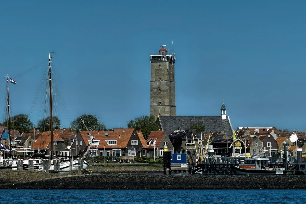 Scenic harbor view featuring traditional Dutch houses and maritime activities under a clear blue sky.