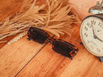 A vintage-inspired style with sunglasses, an alarm clock, and rustic elements on a wooden surface.