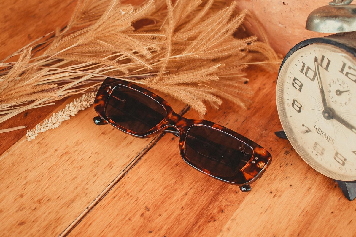 A vintage-inspired style with sunglasses, an alarm clock, and rustic elements on a wooden surface.