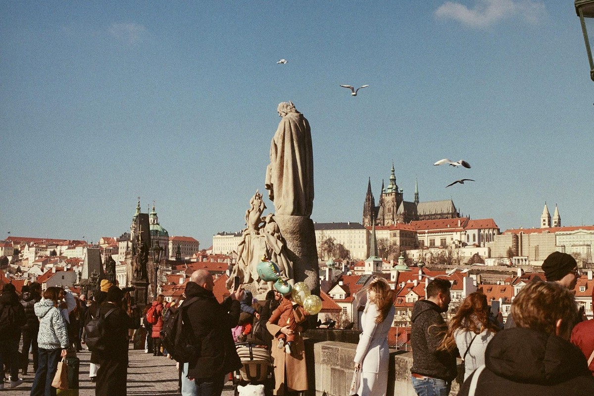 Bustling scene on Charles Bridge, Prague, with tourists and St. Vitus Cathedral in the background.