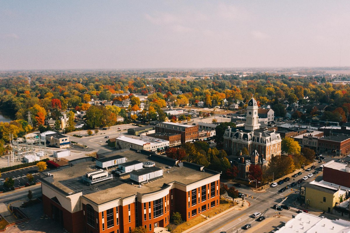 From above of aged building exteriors near roads and river behind bright trees in town in fall