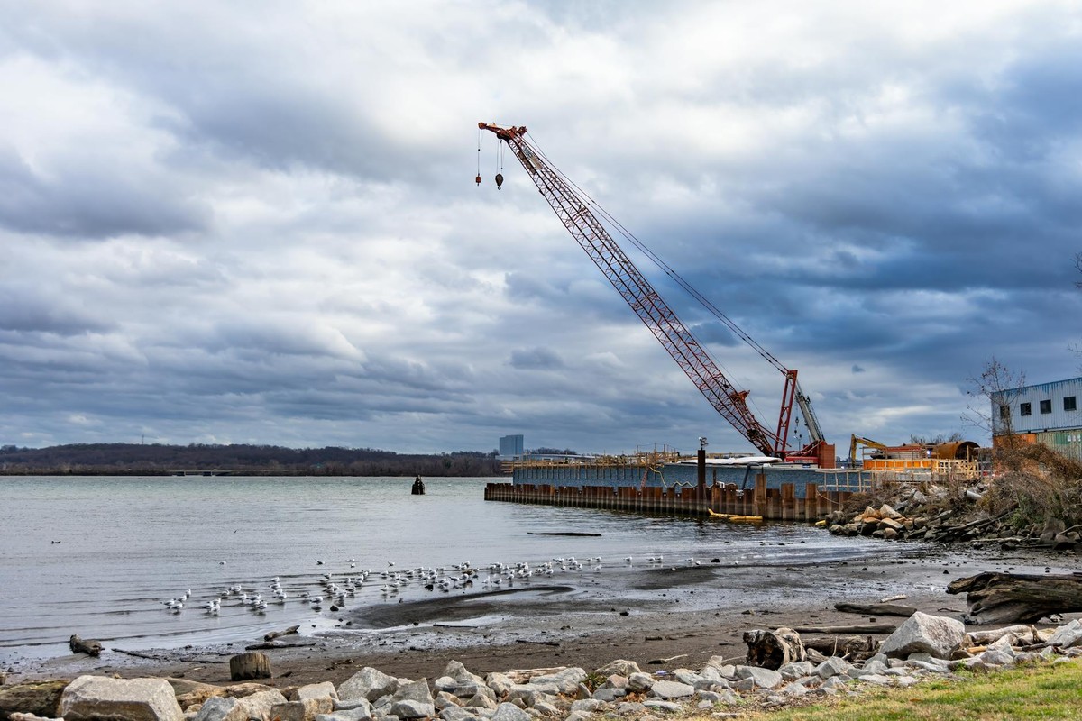 Crane on a waterfront construction site under dramatic cloudy skies.