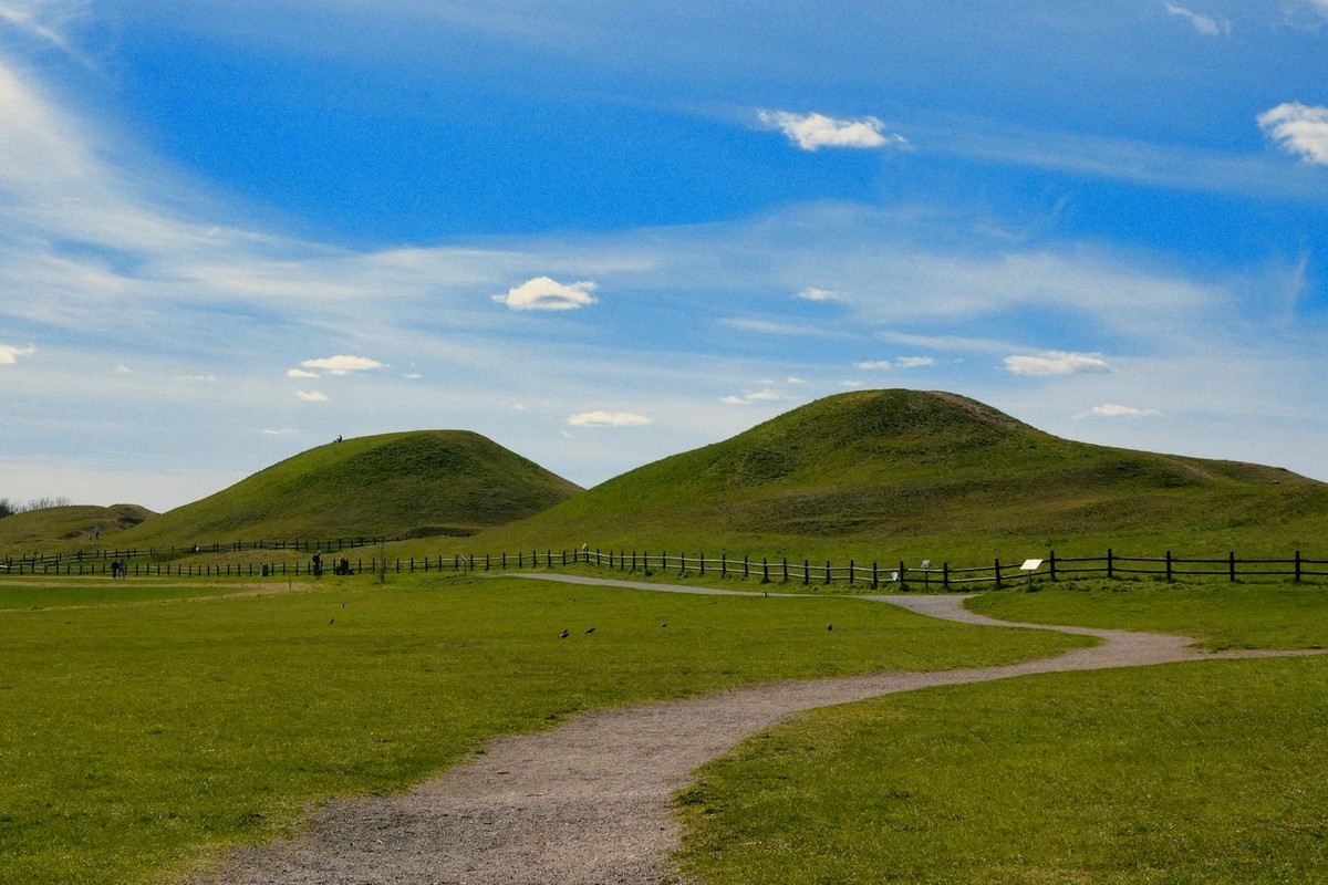 Explore the serene landscape of ancient burial mounds in Sweden under a bright blue sky.