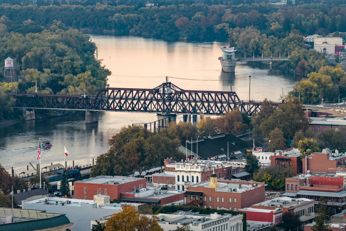 A scenic view of Sacramento's downtown riverfront featuring a historic bridge and colorful autumn foliage.