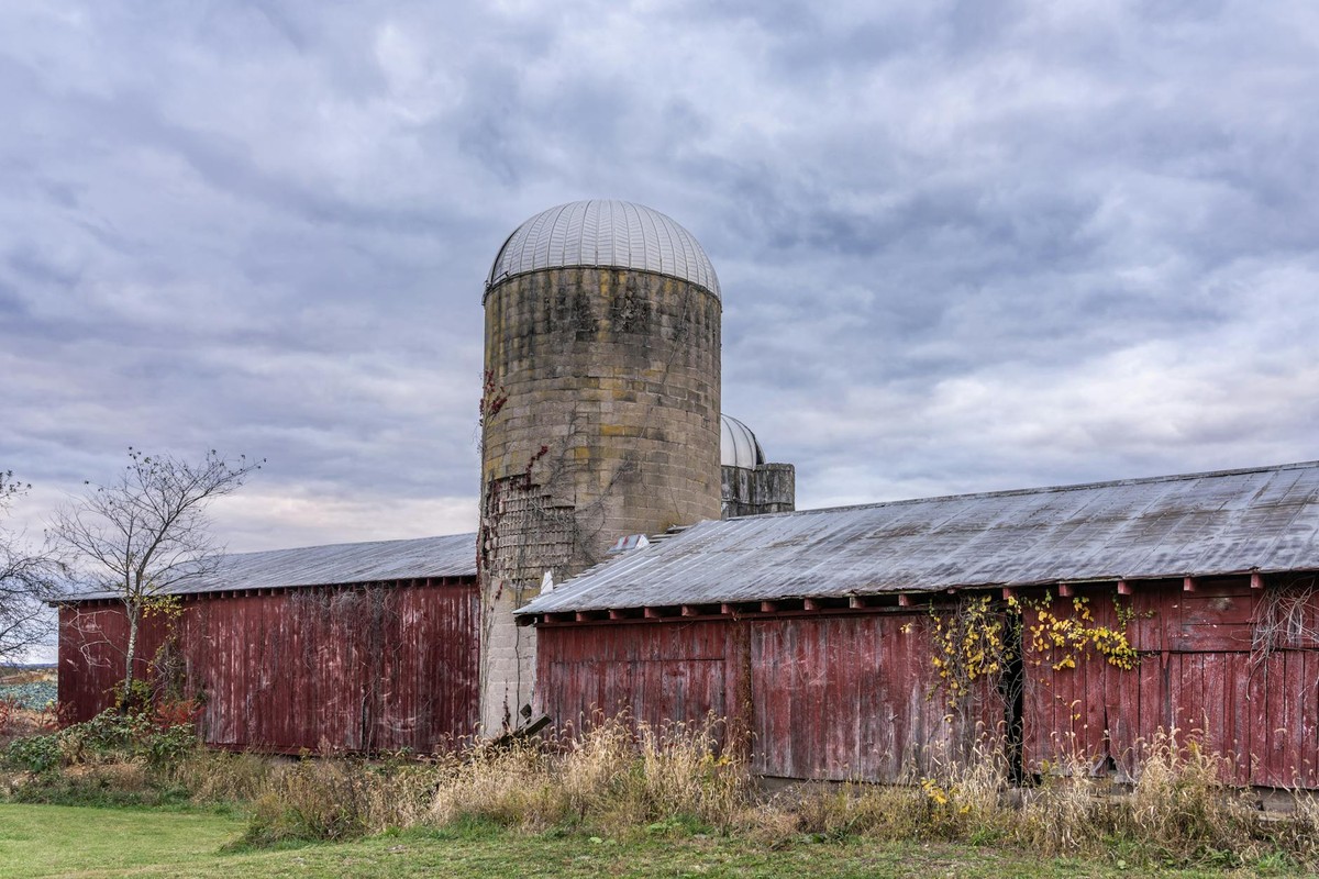 Weathered red barn and silo under cloudy skies in Muncy, Pennsylvania.