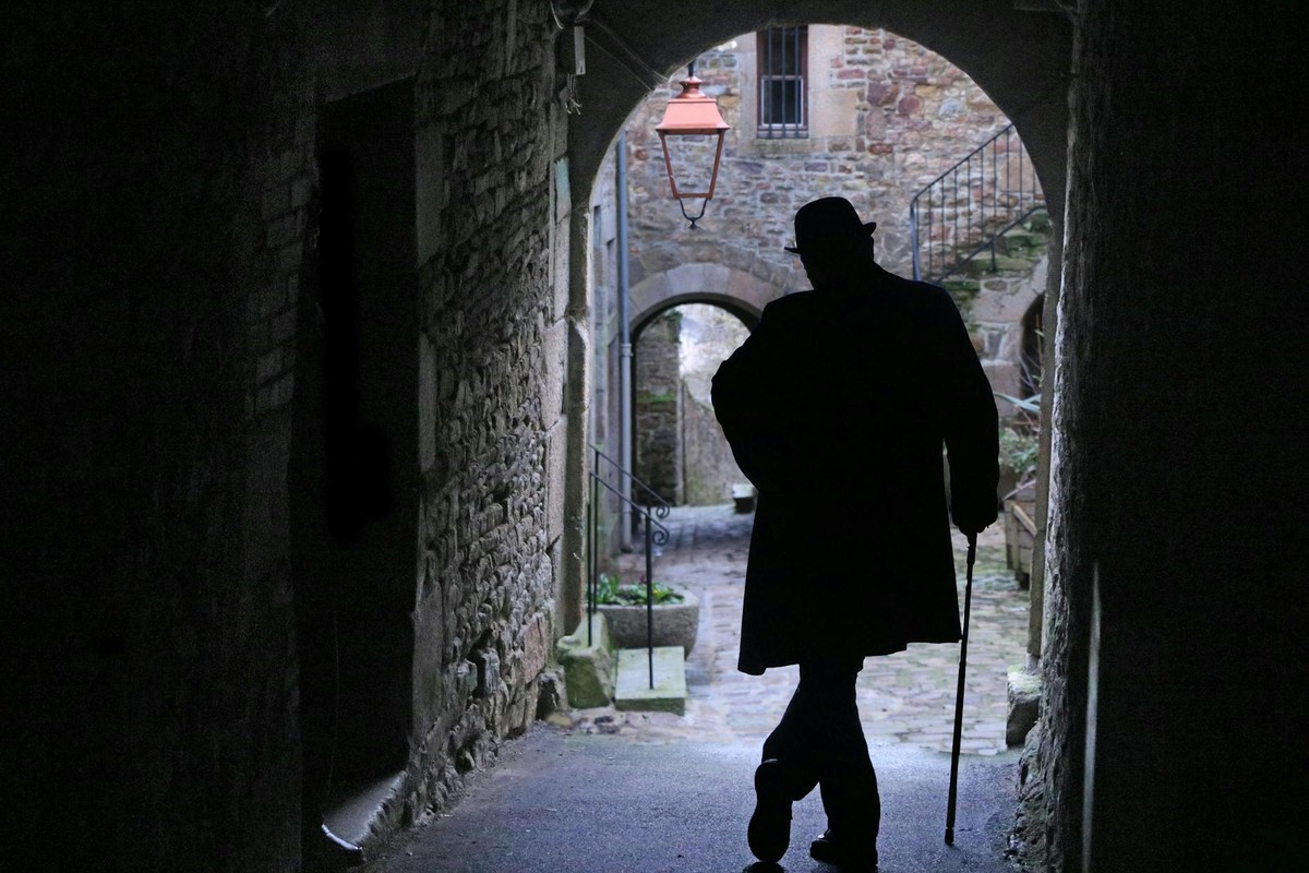 A silhouette of a man with a cane in a historic alley of Villedieu-les-Poêles, France.