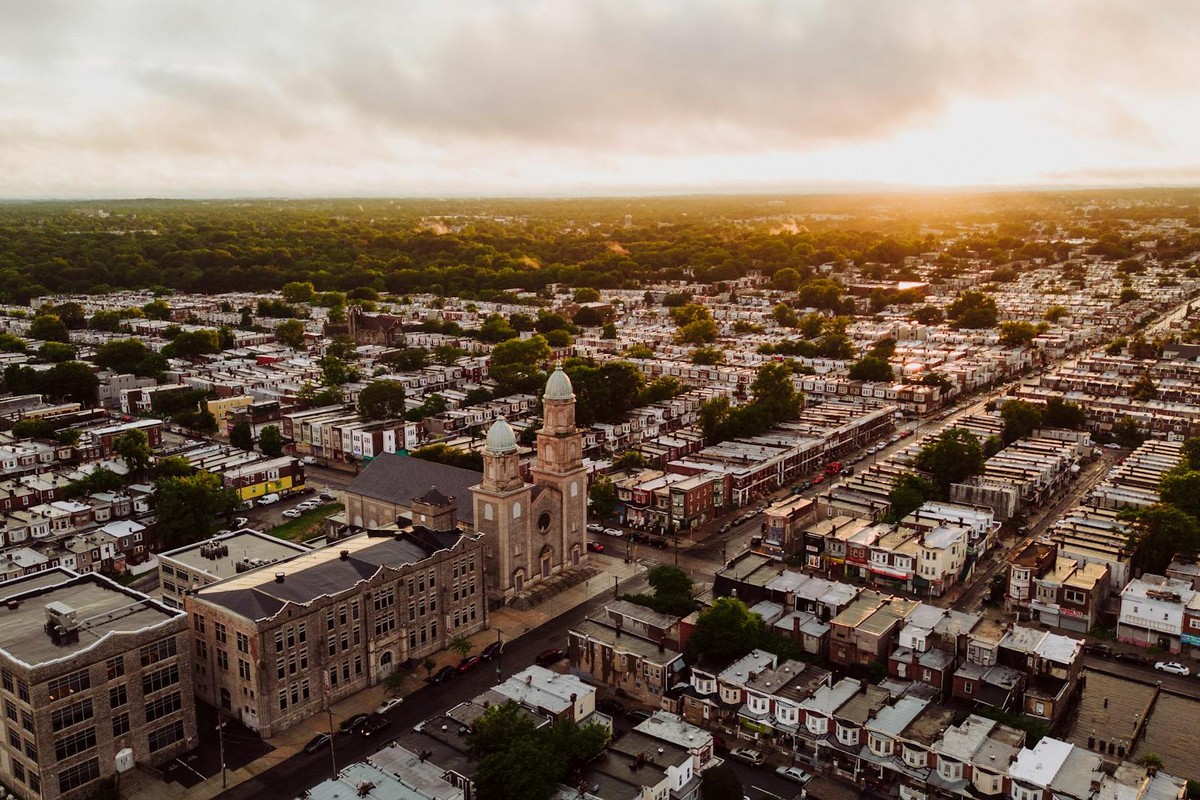 Drone shot of a Philadelphia church and neighborhood at sunset, showcasing urban architecture and green spaces.