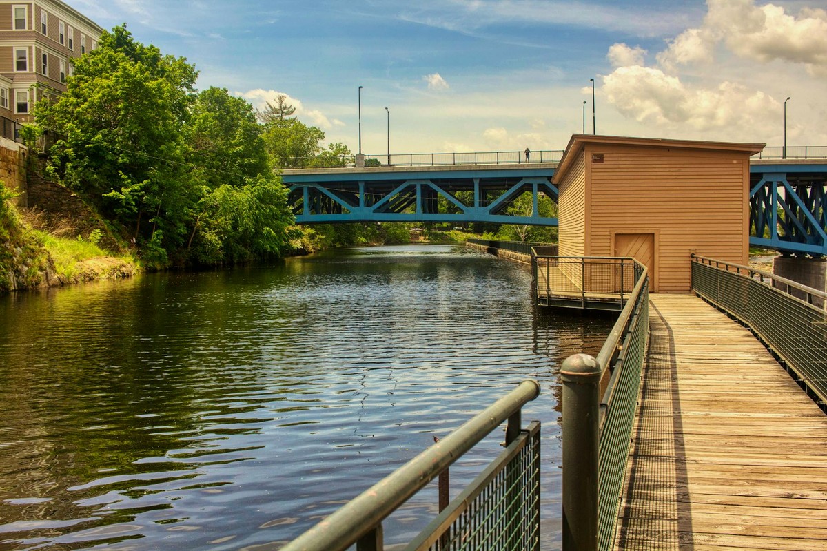 Tranquil urban canal scene with a blue bridge and wooden walkway on a sunny day.