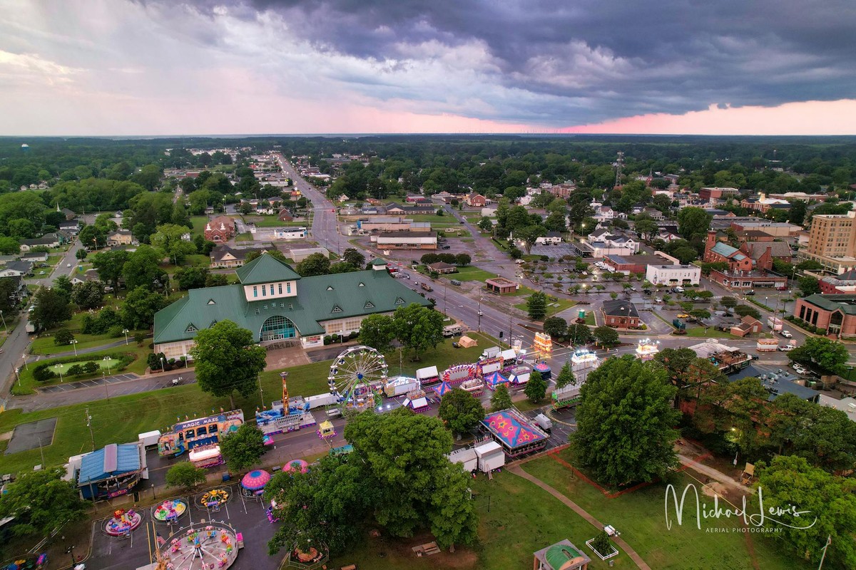 Aerial view showcasing a vibrant town fair with rides and stalls during dusk, under dramatic skies.