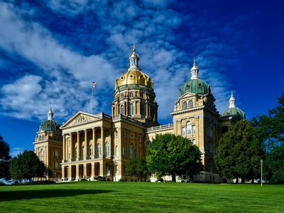Majestic Iowa State Capitol with golden dome and lush green lawn on a clear sunny day.