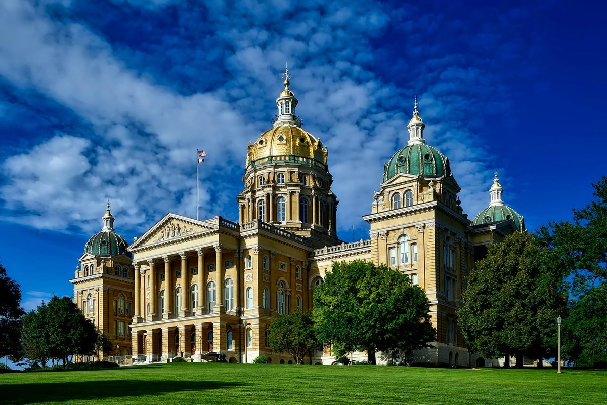 Majestic Iowa State Capitol with golden dome and lush green lawn on a clear sunny day.