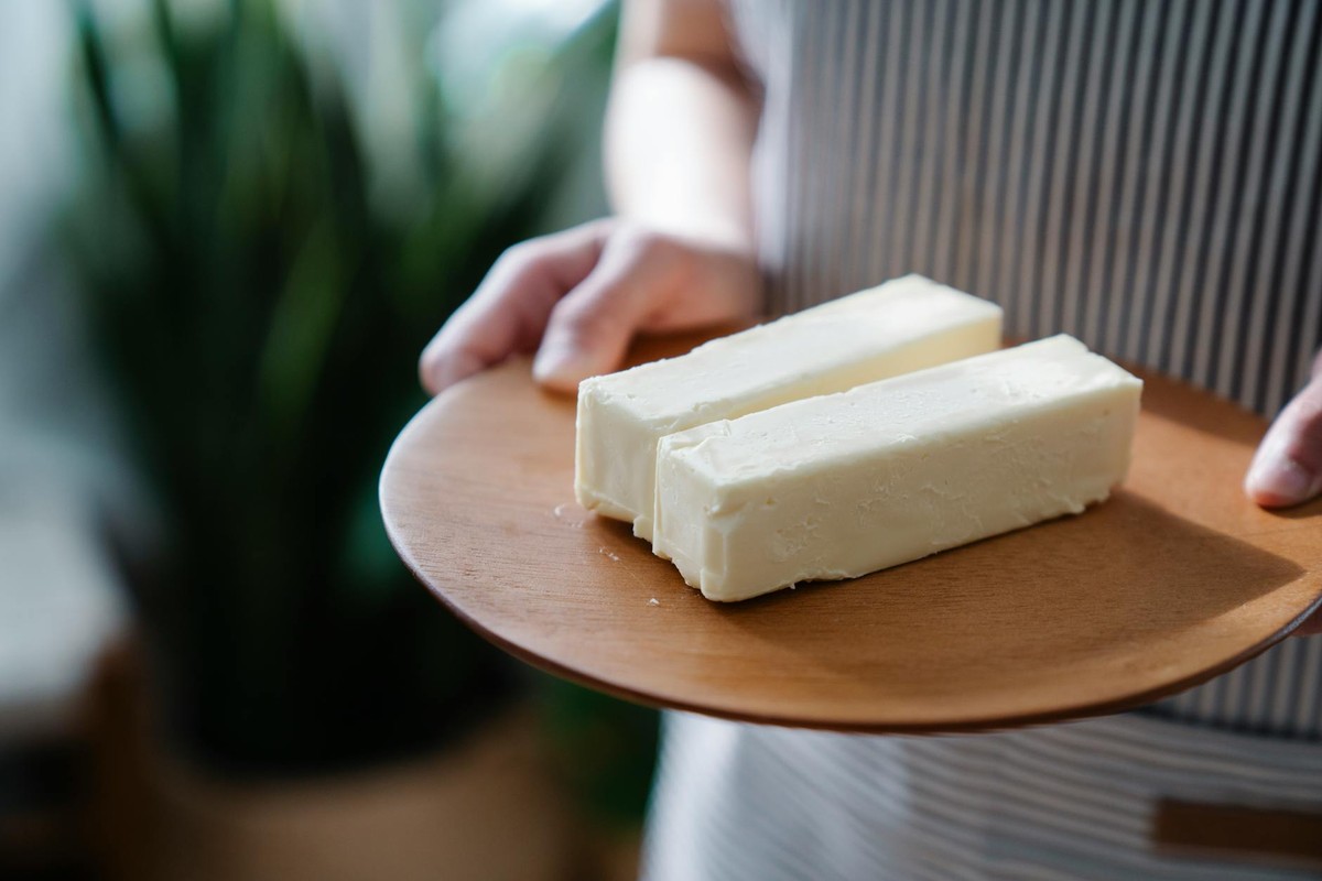 Close-up of hands holding a wooden plate with two sticks of butter.