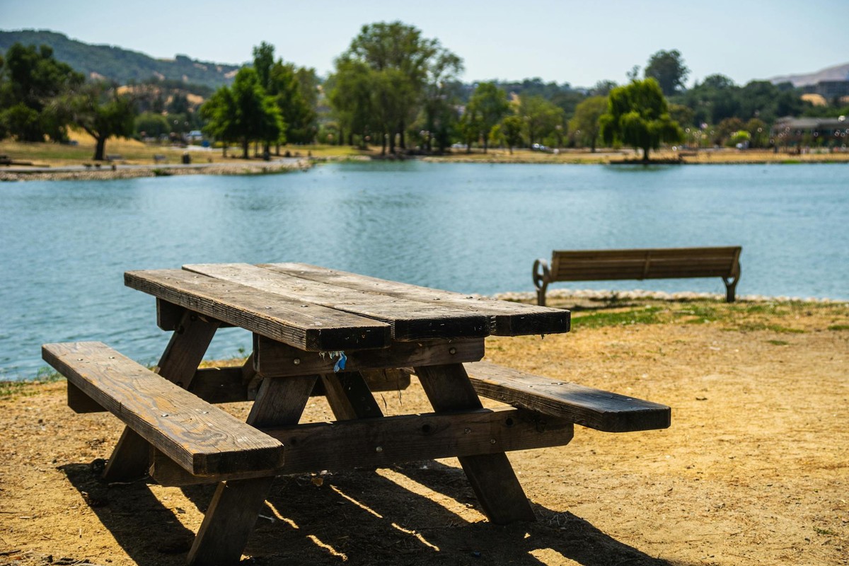 A wooden picnic table by a serene lake, perfect for summer relaxation and leisure.