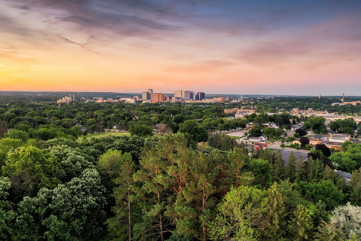 Breathtaking aerial view of Rochester, MN skyline surrounded by lush greenery at sunset.