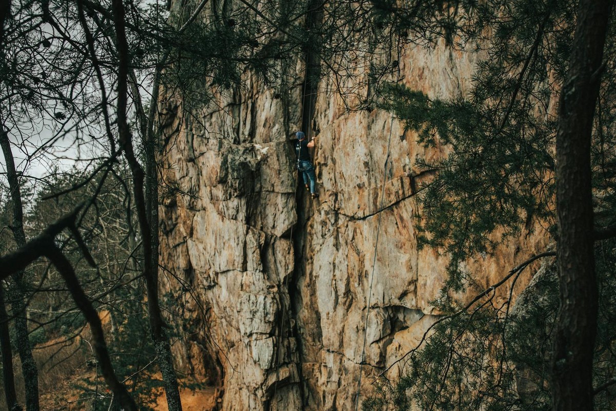 A climber ascends a rocky cliff surrounded by trees in Gastonia, NC.