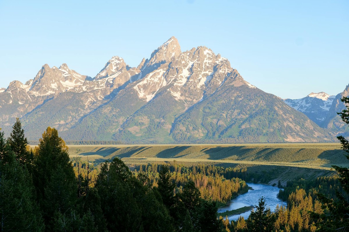 Stunning view of the Grand Teton mountains with a river flowing through lush greenery in Wyoming.