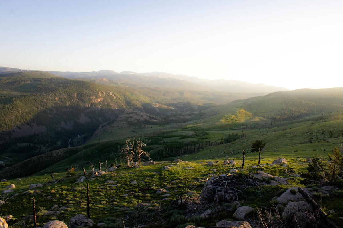 Picturesque mountain landscape during sunrise in Wyoming with rolling hills and lush greenery.