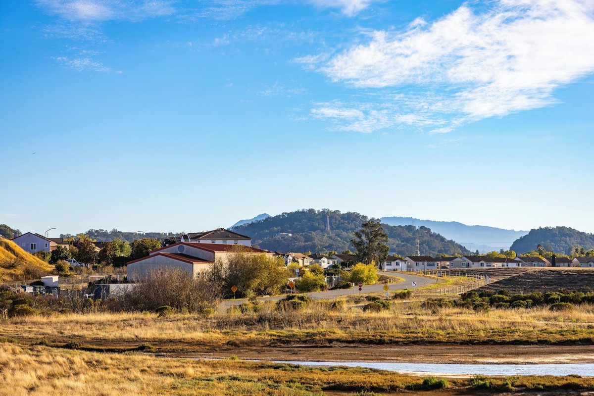 Beautiful rural landscape with houses, open fields, and distant mountains under a blue sky.