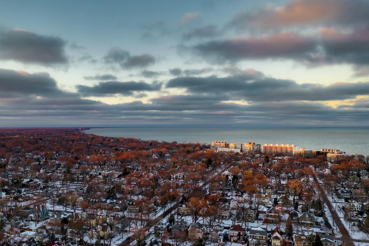 Drone view of residential buildings with autumn trees against endless sea under cloudy sky in evening