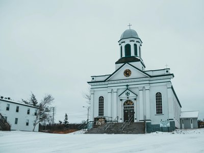 Facade of St Josephs church with clock and crosses located on snowy street near building in St Georges on winter day