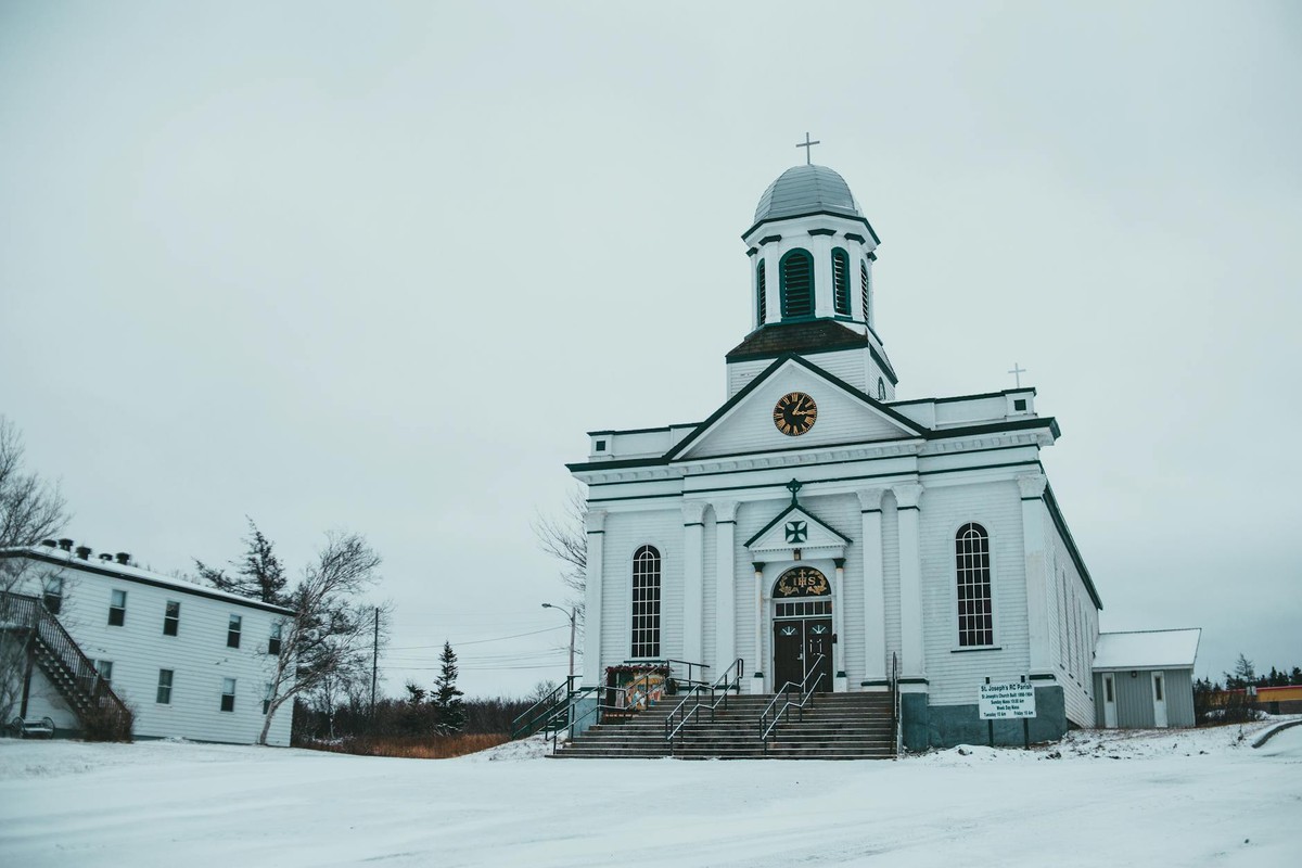 Facade of St Josephs church with clock and crosses located on snowy street near building in St Georges on winter day