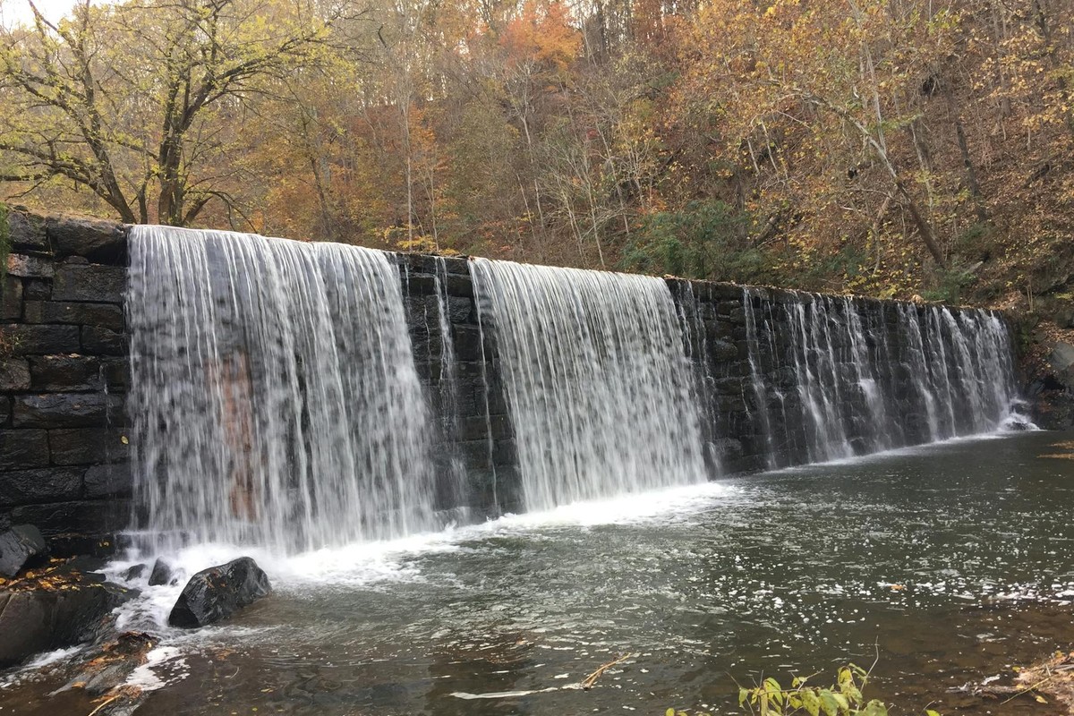 Beautiful waterfall cascading over a stone wall surrounded by fall foliage in Lynchburg, Virginia.